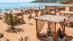 A beach with wooden structures, some with canopies, and a few people relaxing. - Aelia Apartments (Andros)