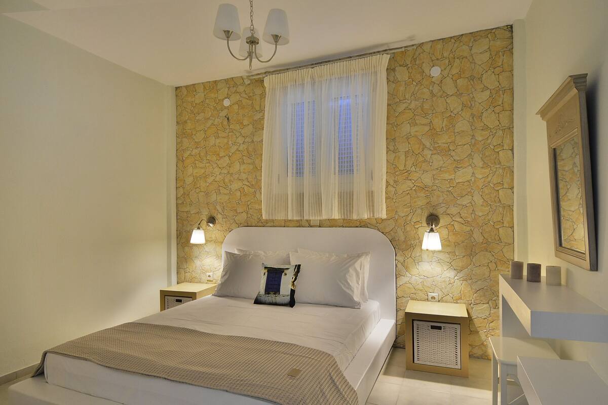 A bedroom with a stone wall, a bed with white bedding, two bedside lamps, and a chandelier.