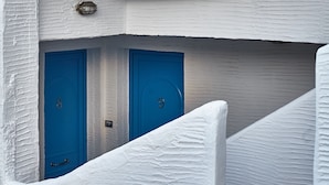 A white building with two blue doors, a stone floor, and a small staircase. - Aelia Apartments (Andros)