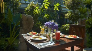 A table set outdoors with a variety of breakfast items, including eggs, toast, and fruit, along with a drink and a vase of flowers. - Bumi Muwa Ubud (Ubud)
