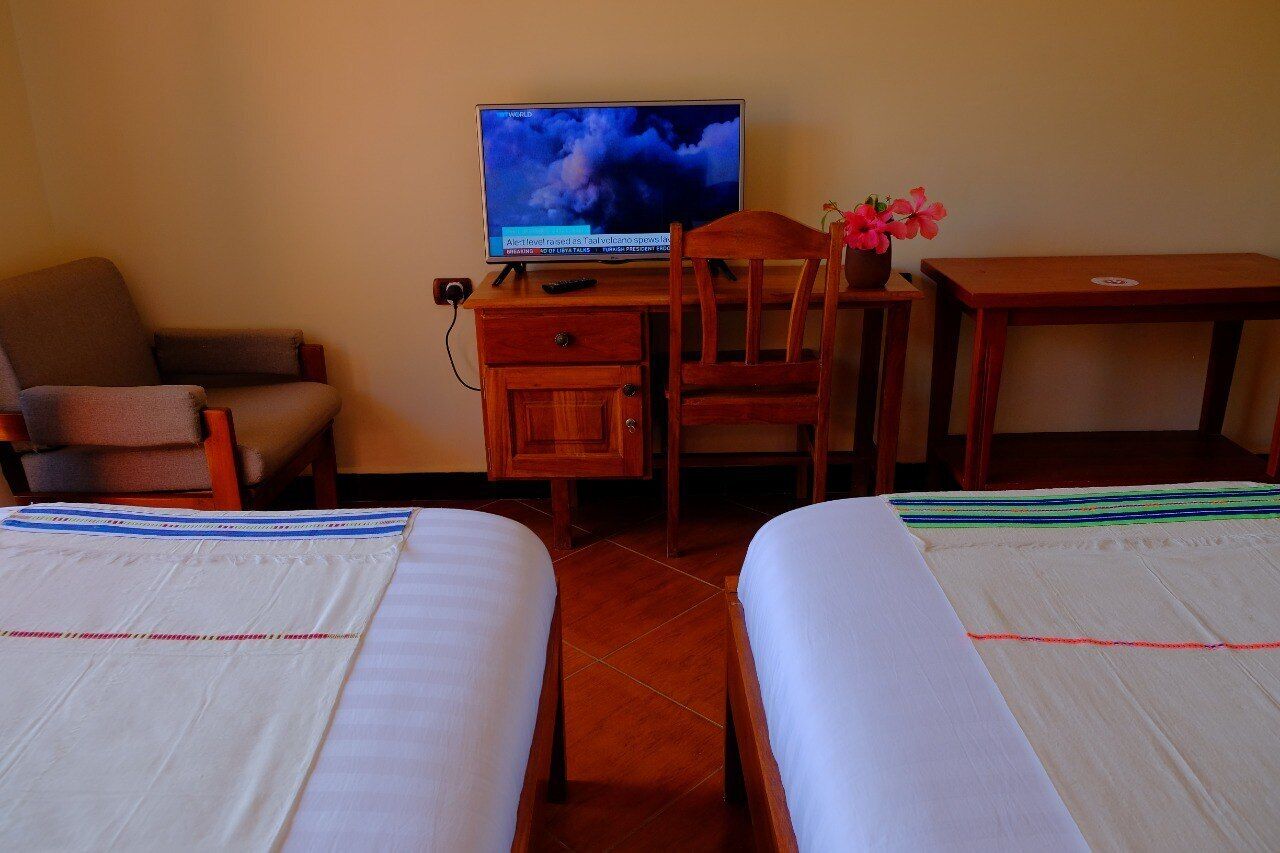 A hotel room with two beds, a desk with a television, a chair, and a small table with a flower vase.