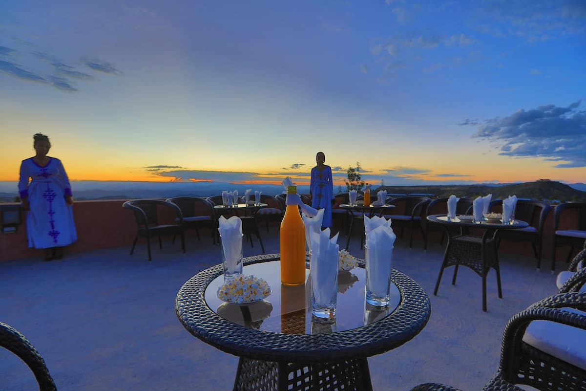 An outdoor seating area with round tables, chairs, and a view of the sunset.