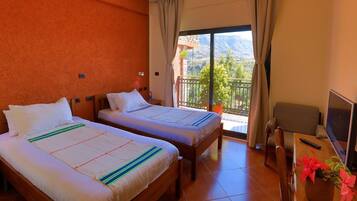 Habitación de hotel con dos camas, un balcón con vistas, un escritorio y una silla, y un televisor.