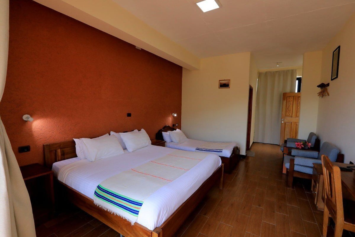 A hotel room with two beds, wooden headboards, a small table, and a chair.