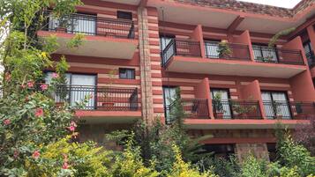 A multi-story building with balconies, brick walls, and various plants.
