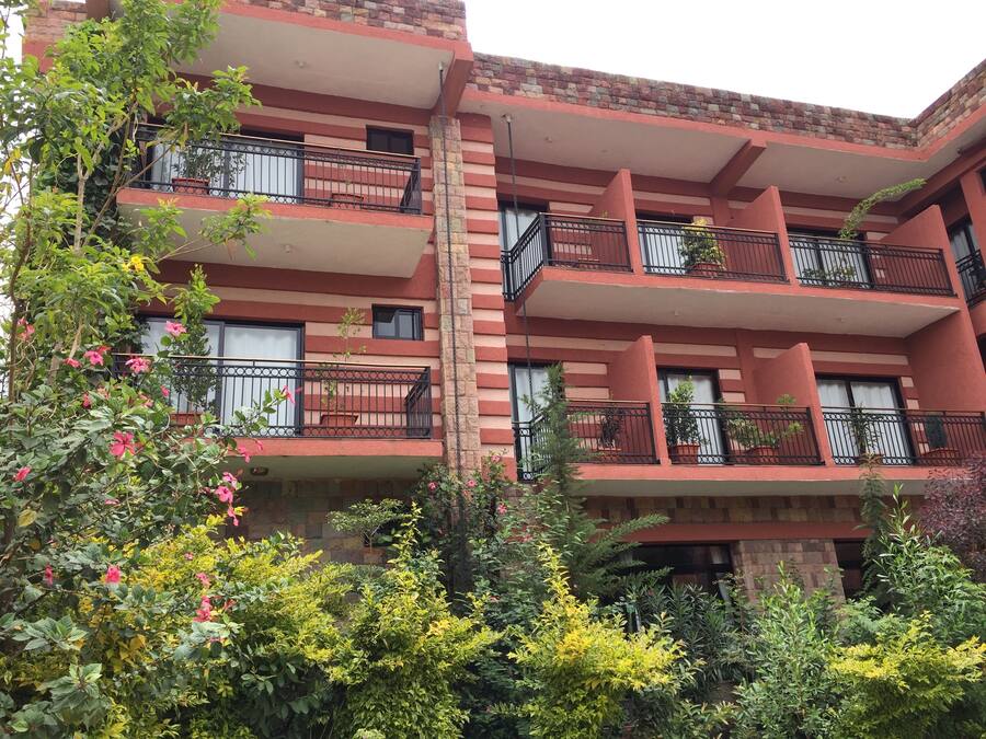 A multi-story building with balconies, brick walls, and various plants.