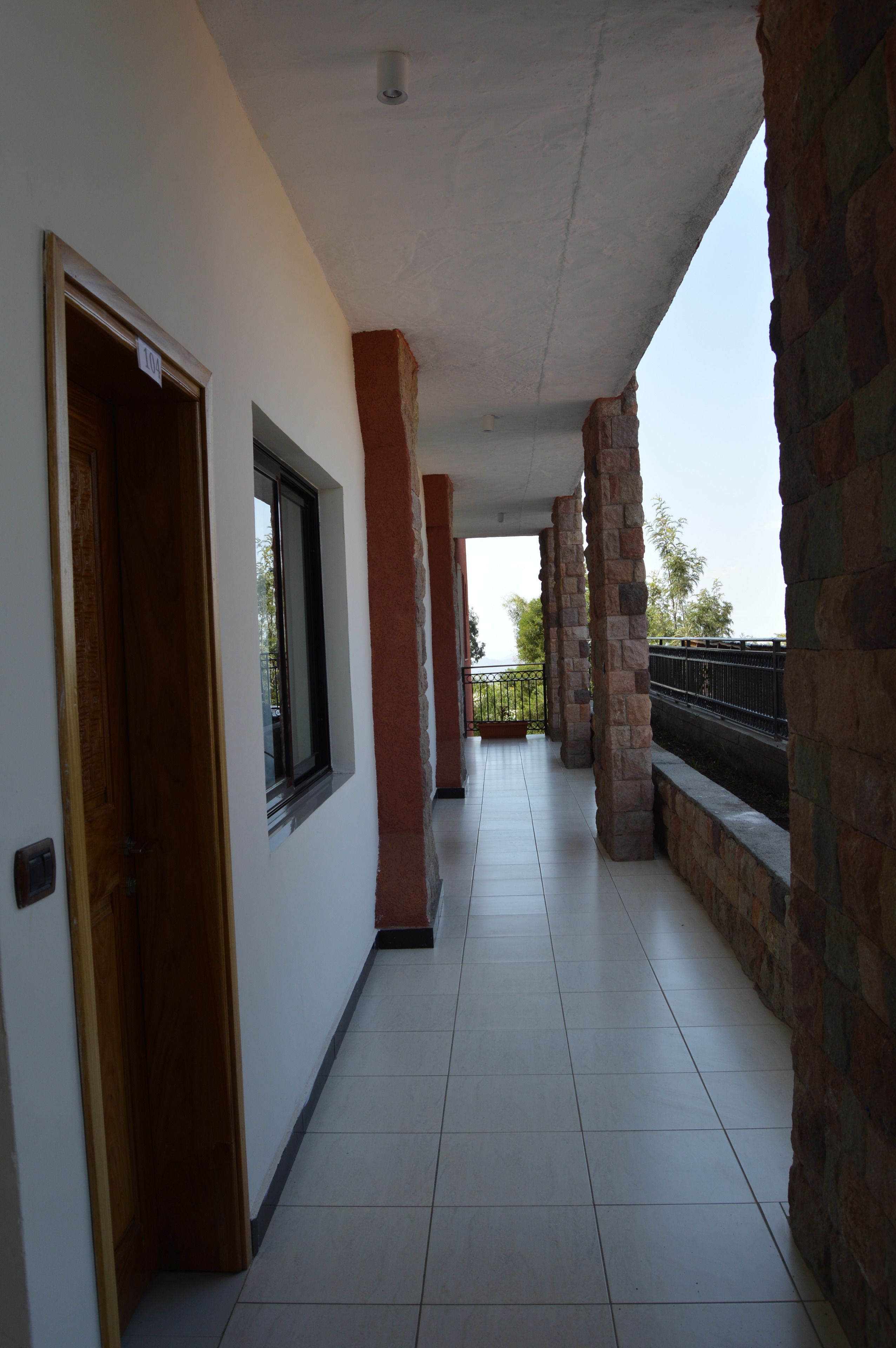 A corridor with a tiled floor, a wooden door, a window, and a balcony with stone pillars.