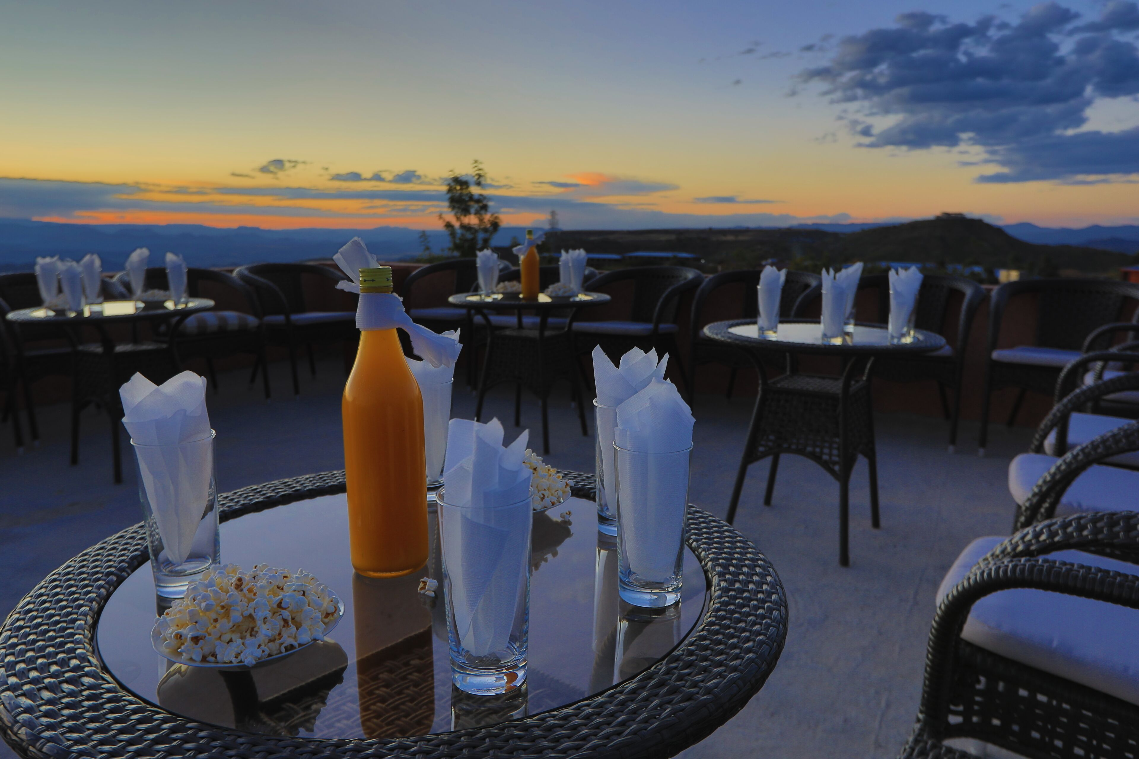 A rooftop dining area with tables set for two, each with a bottle, glasses, and napkins.
