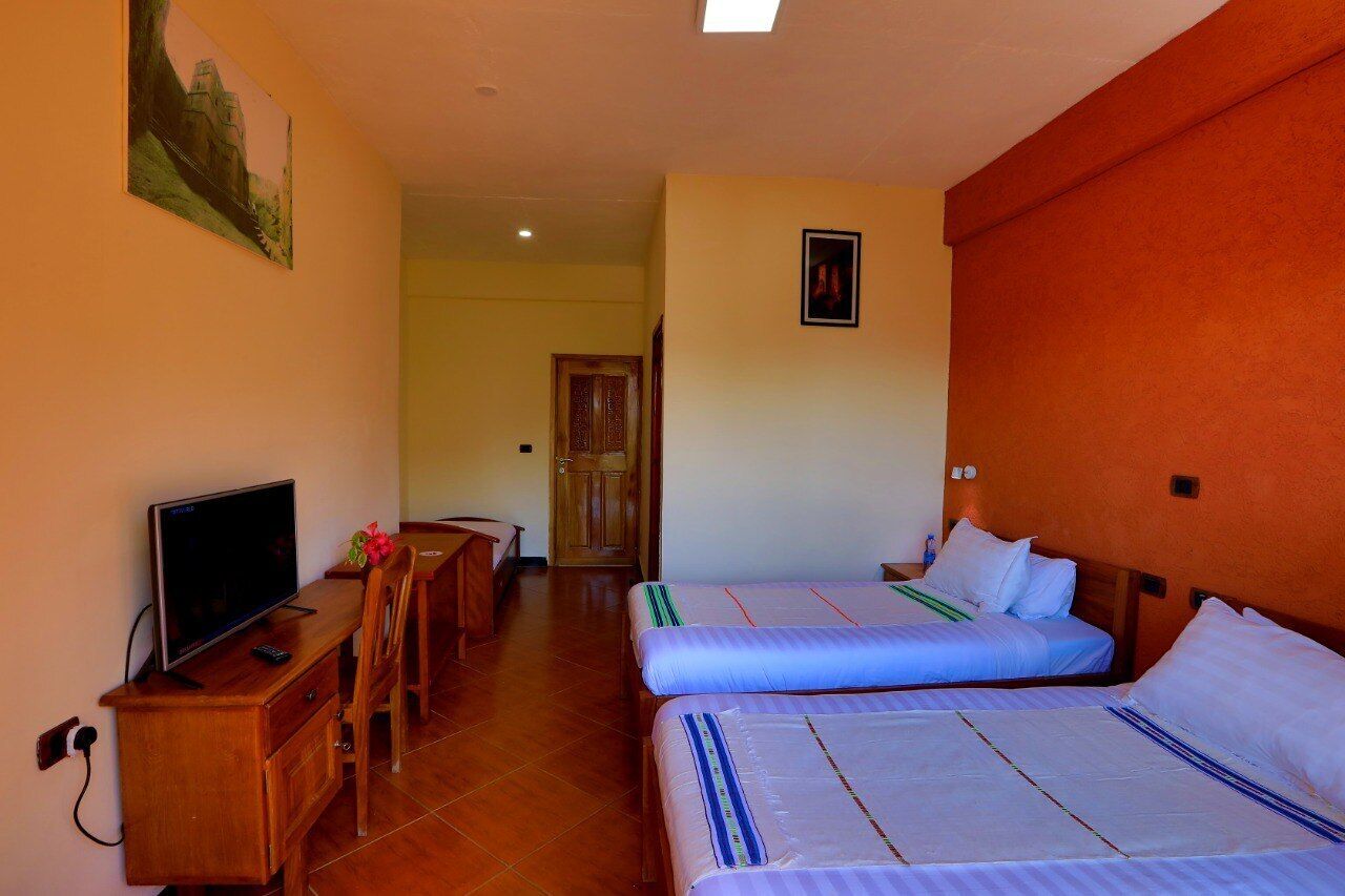 Habitación de hotel con dos camas, un escritorio con televisor y una silla de madera.