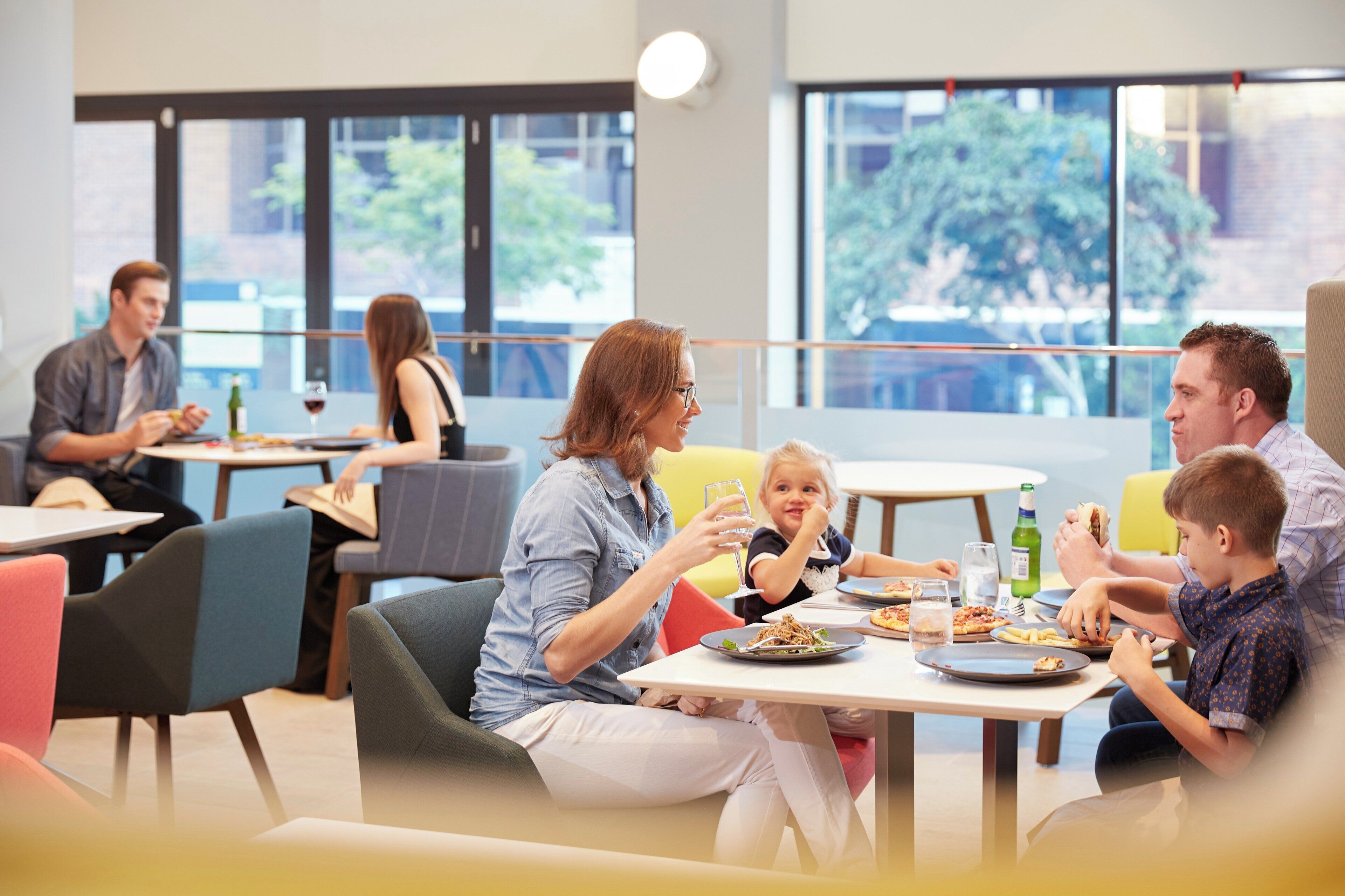 A group of people dining in a modern indoor setting with large windows and a casual atmosphere.