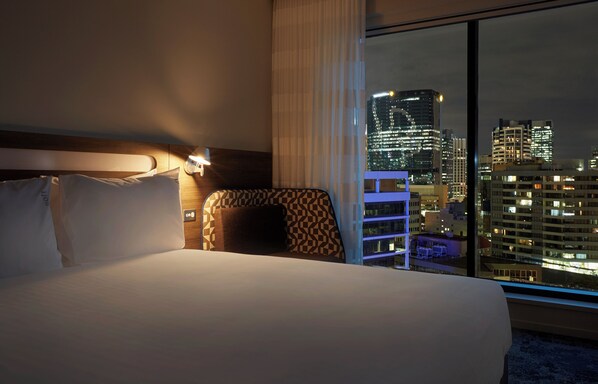 A hotel room with a large bed, a nightstand, and a view of a cityscape at night. - Holiday Inn Express Brisbane Central by IHG (Spring Hill)