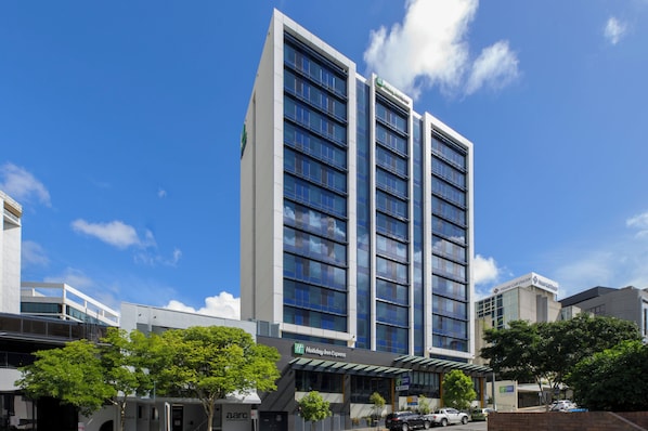 Un hôtel Holiday Inn Express à plusieurs étages, doté d’une façade moderne en verre, situé dans un environnement urbain sous un ciel dégagé.