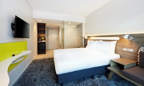 A modern hotel room with a large bed, a flat-screen TV mounted on the wall, a small kitchenette, and a glass shower enclosure. - Holiday Inn Express Brisbane Central by IHG (Spring Hill)