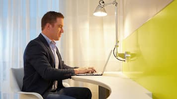 A man sitting at a desk with a laptop, a desk lamp, and a green accent wall.