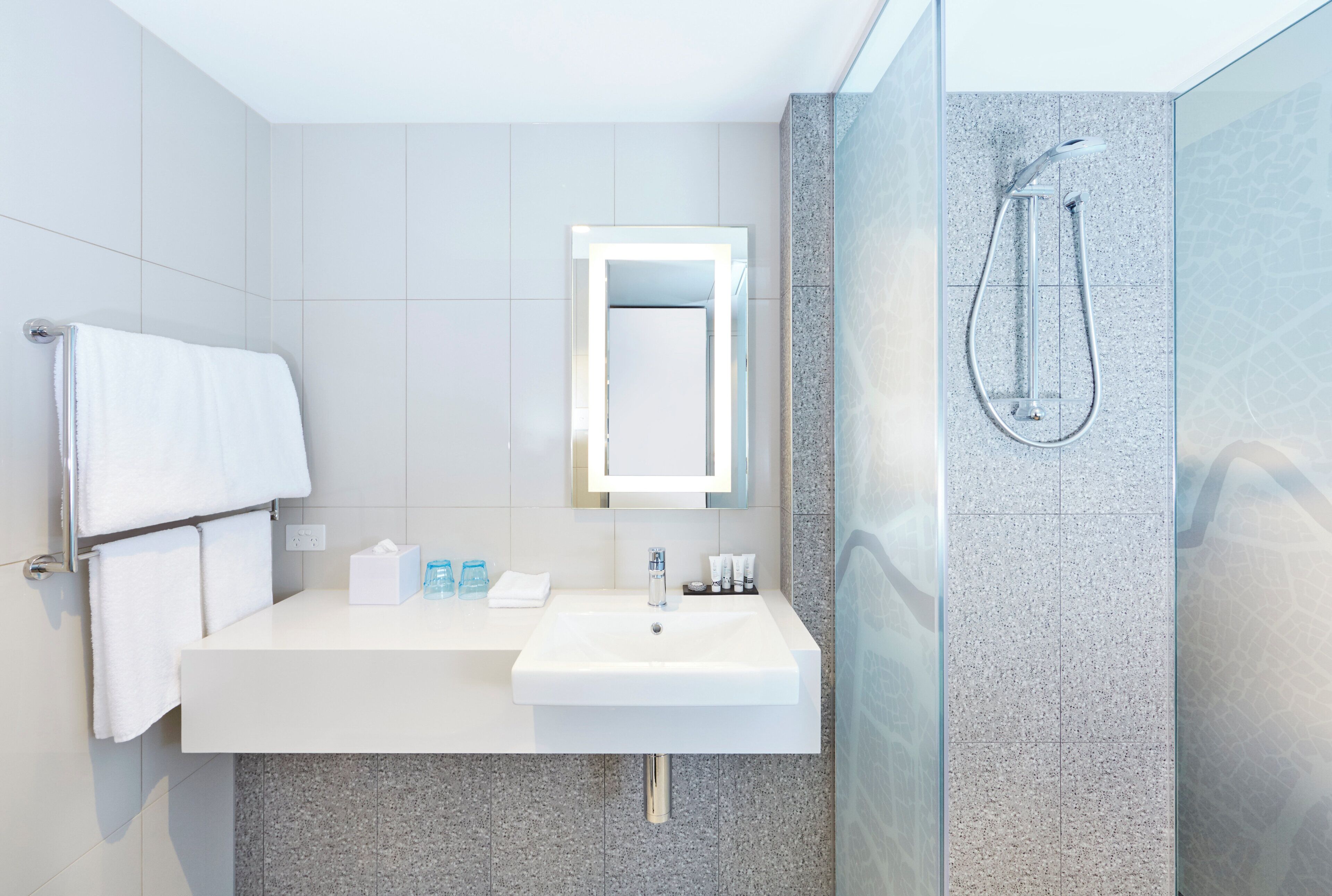 A modern bathroom with a white sink, a mirror, a towel rack, and a shower with a glass door.