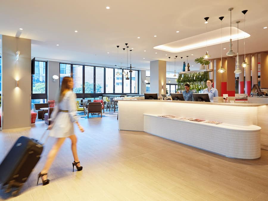 Un hall d’hôtel moderne avec un comptoir d’accueil, un espace salon et de grandes fenêtres.