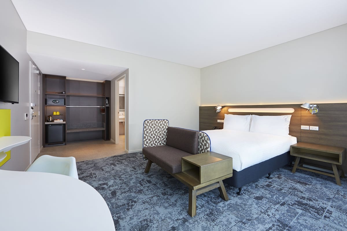 Une chambre d’hôtel comprenant un lit, des tables de chevet, une télévision, un coin salon et une kitchenette.
