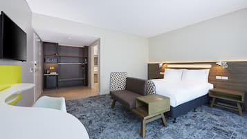 A hotel room with a bed, bedside tables, a TV, a seating area, and a kitchenette.