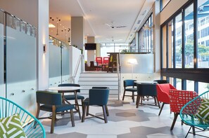 A modern interior with a staircase leading to an upper level, seating area with tables and chairs, and large windows offering views of the outside. - Holiday Inn Express Brisbane Central by IHG (Spring Hill)