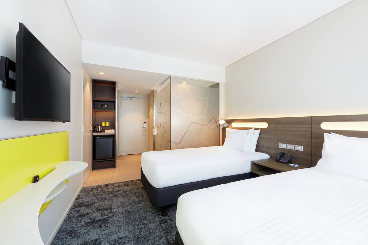 Une chambre d’hôtel moderne équipée de deux lits, d’un téléviseur à écran plat, d’un bureau et d’une salle de bain avec douche.
