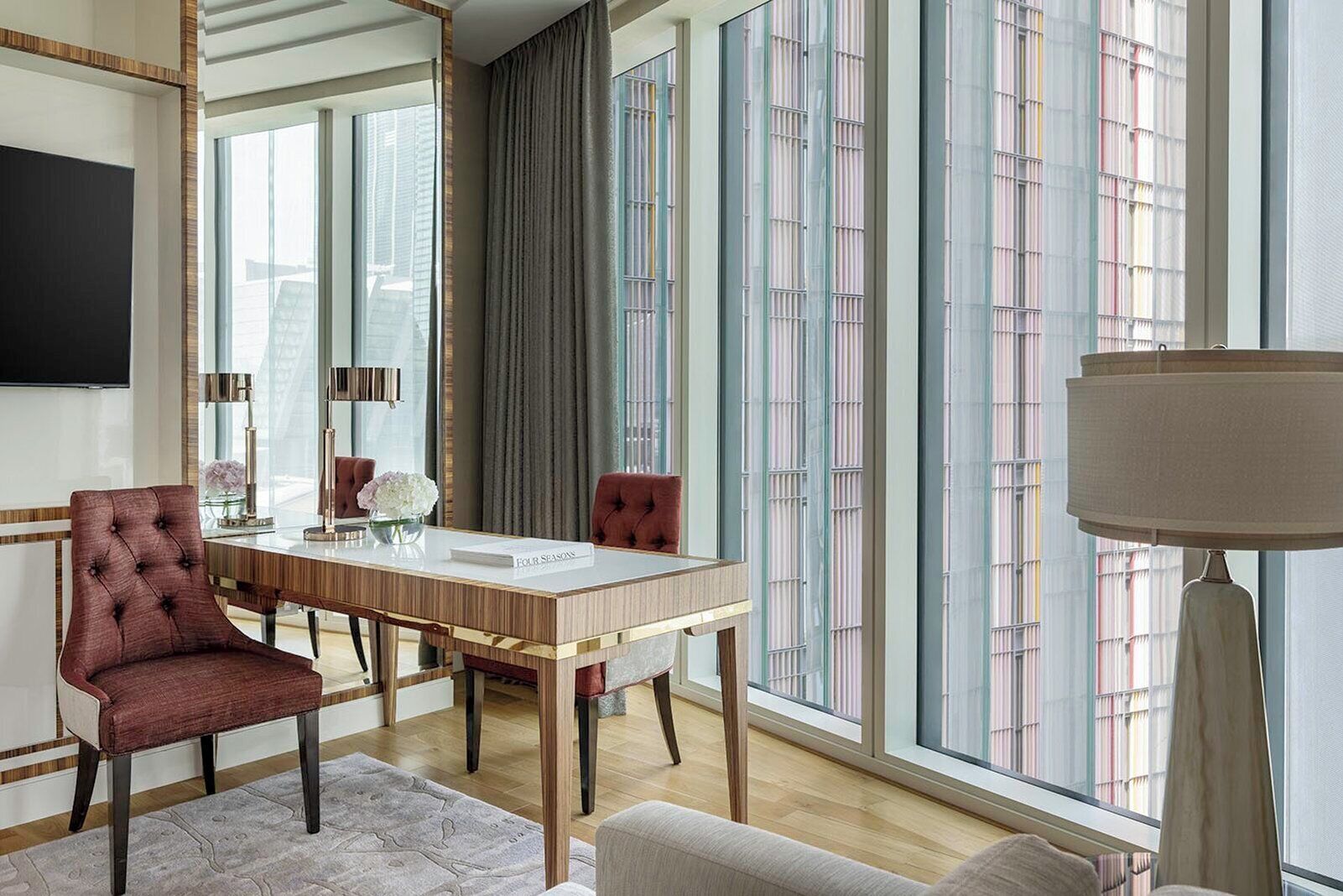 Un espace repas moderne avec une table en bois, des chaises à revêtement rouge et de grandes fenêtres équipées de stores verticaux.