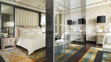 A luxurious bedroom with a large bed, a nightstand, a mirror, and a seating area with a sofa and armchairs.