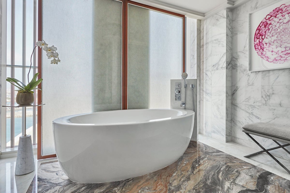 Ein modernes Badezimmer mit freistehender Badewanne, Marmorboden und einem großen Fenster mit Blick.