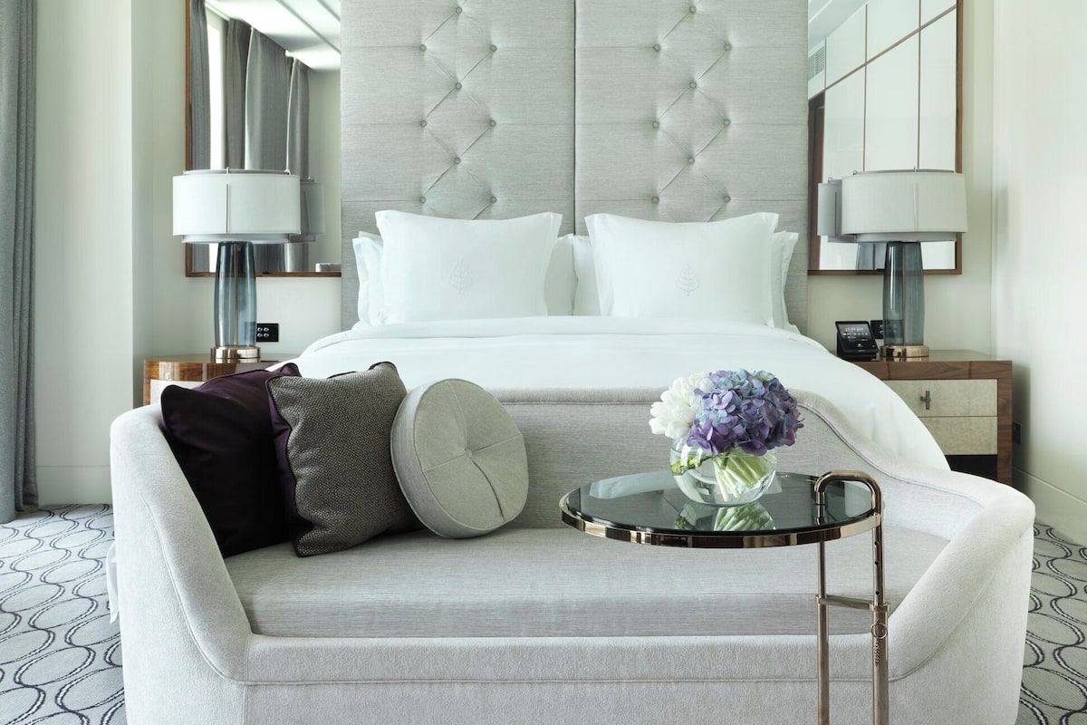 Ein Hotelzimmer mit einem großen Bett, einem Sofa, einem kleinen runden Tisch mit Blumenvase und zwei Nachttischlampen.