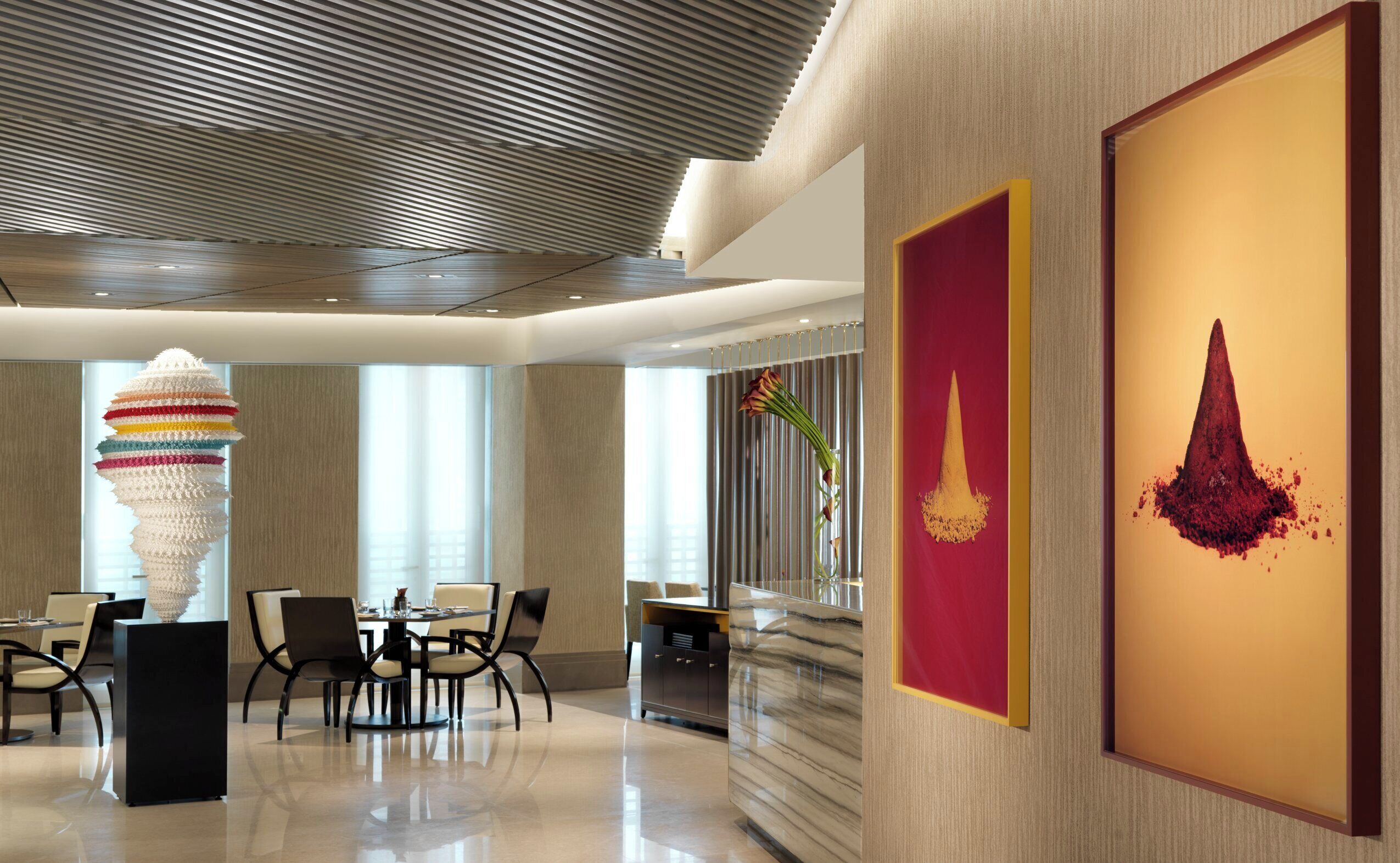 Un hall d’hôtel moderne doté d’un espace repas, d’une sculpture originale et d’œuvres d’art encadrées qui ornent les murs.