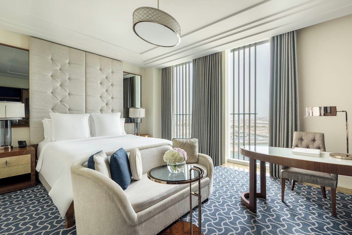 Ein Hotelzimmer mit einem großen Bett, einer Couch, einem Esstisch und Blick auf die Stadt.