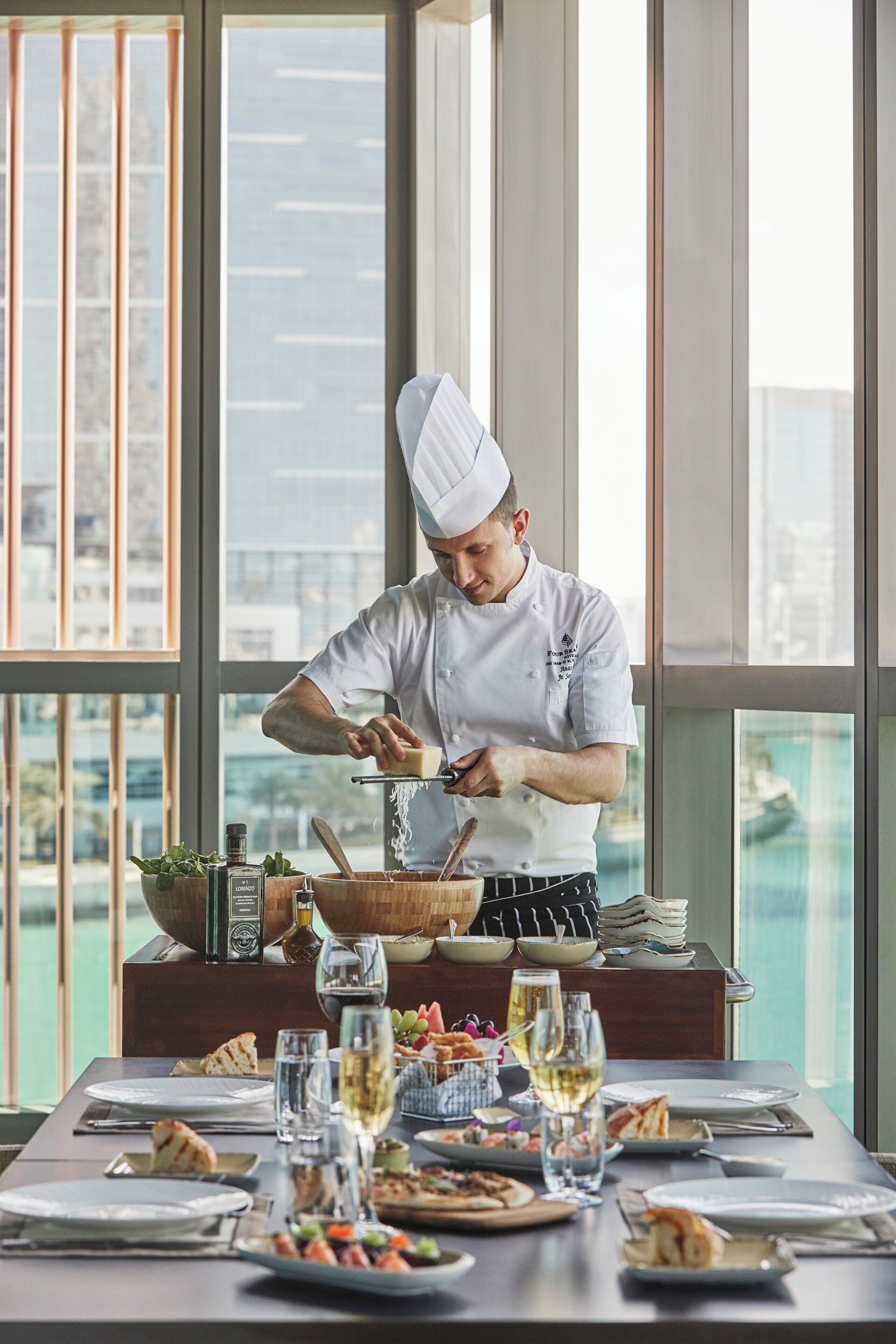 A chef preparing food in a modern kitchen with large windows overlooking a cityscape.