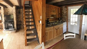 A rustic kitchen with wooden cabinets, a stone fireplace, and a wooden staircase.