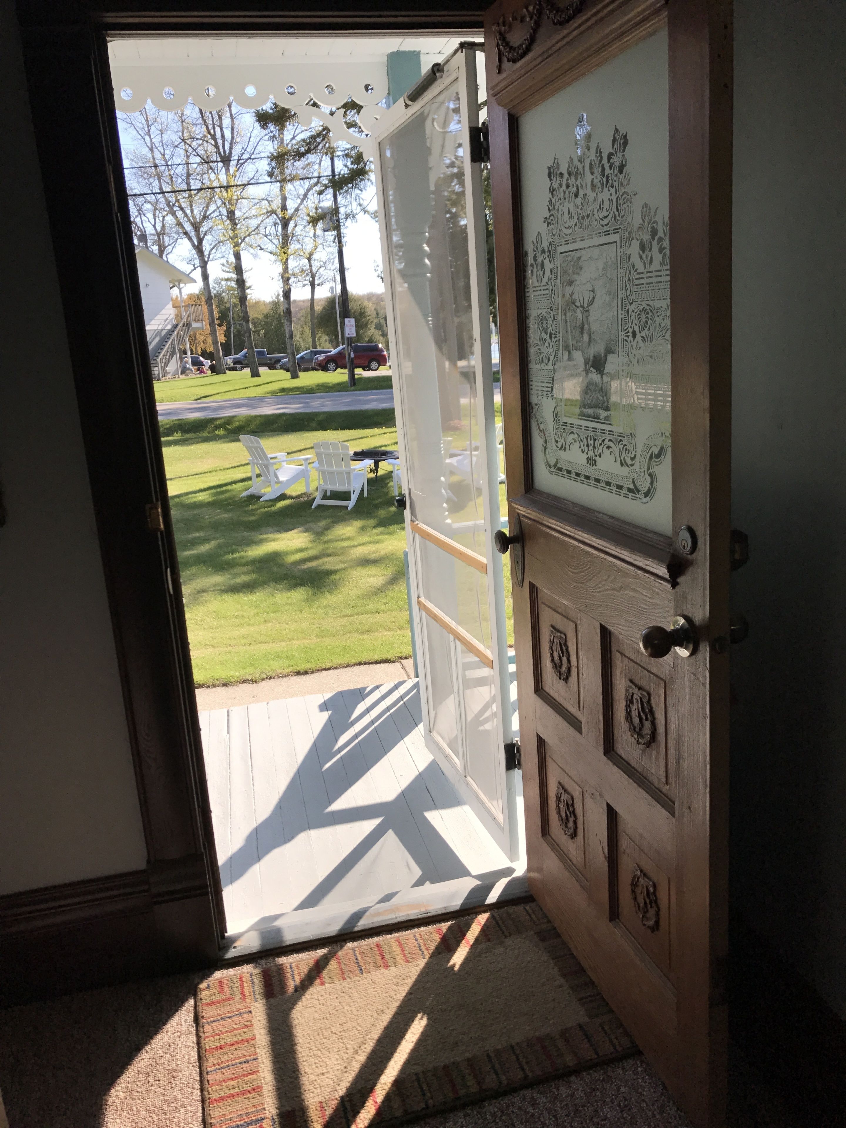 An open door leading to a grassy outdoor area with white chairs and a decorative wall with carved designs.