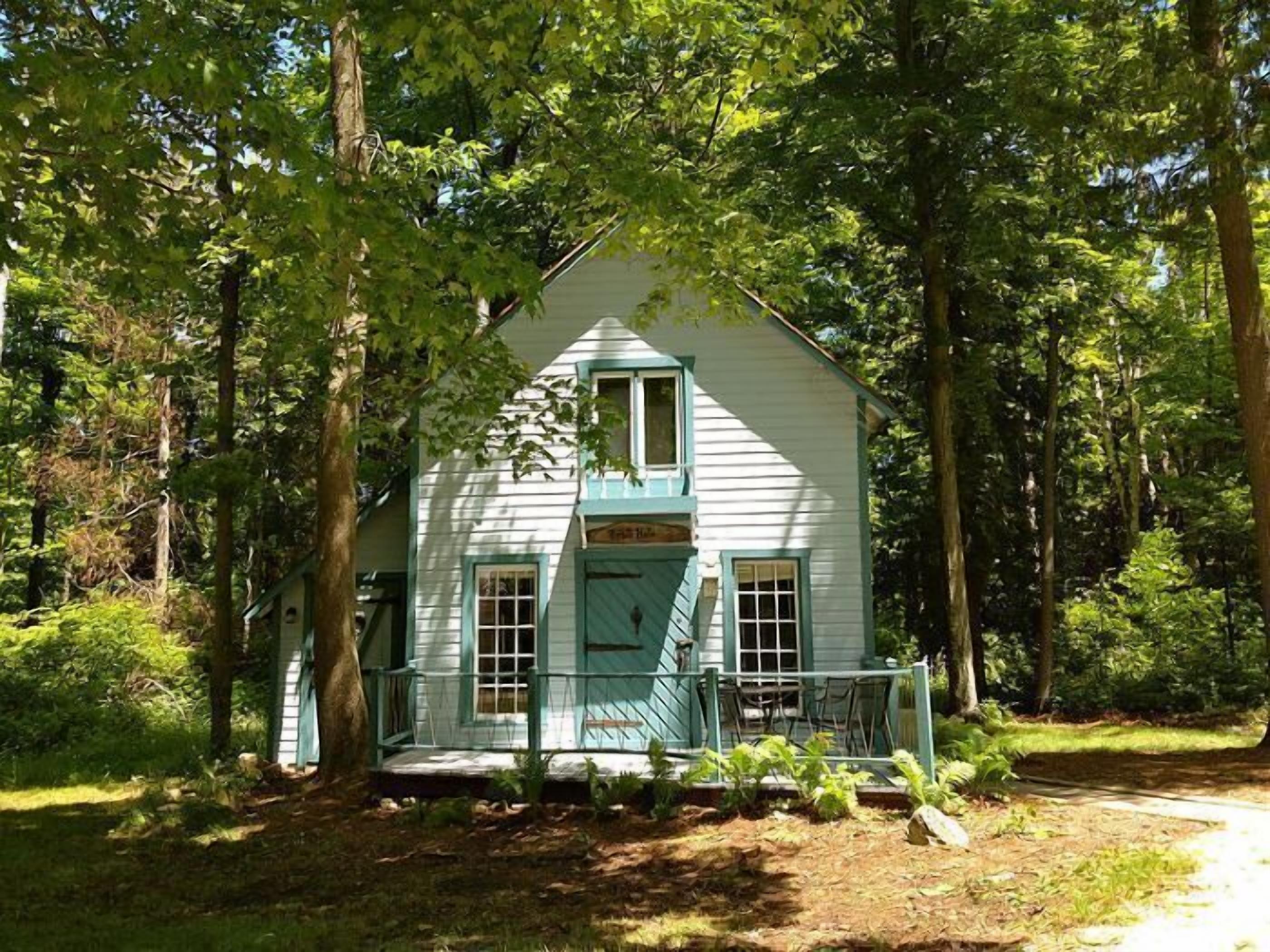 A white house with a blue door and windows, surrounded by trees.