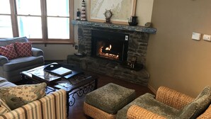 A cozy living room with a stone fireplace, a sofa, a coffee table, and a wicker ottoman.