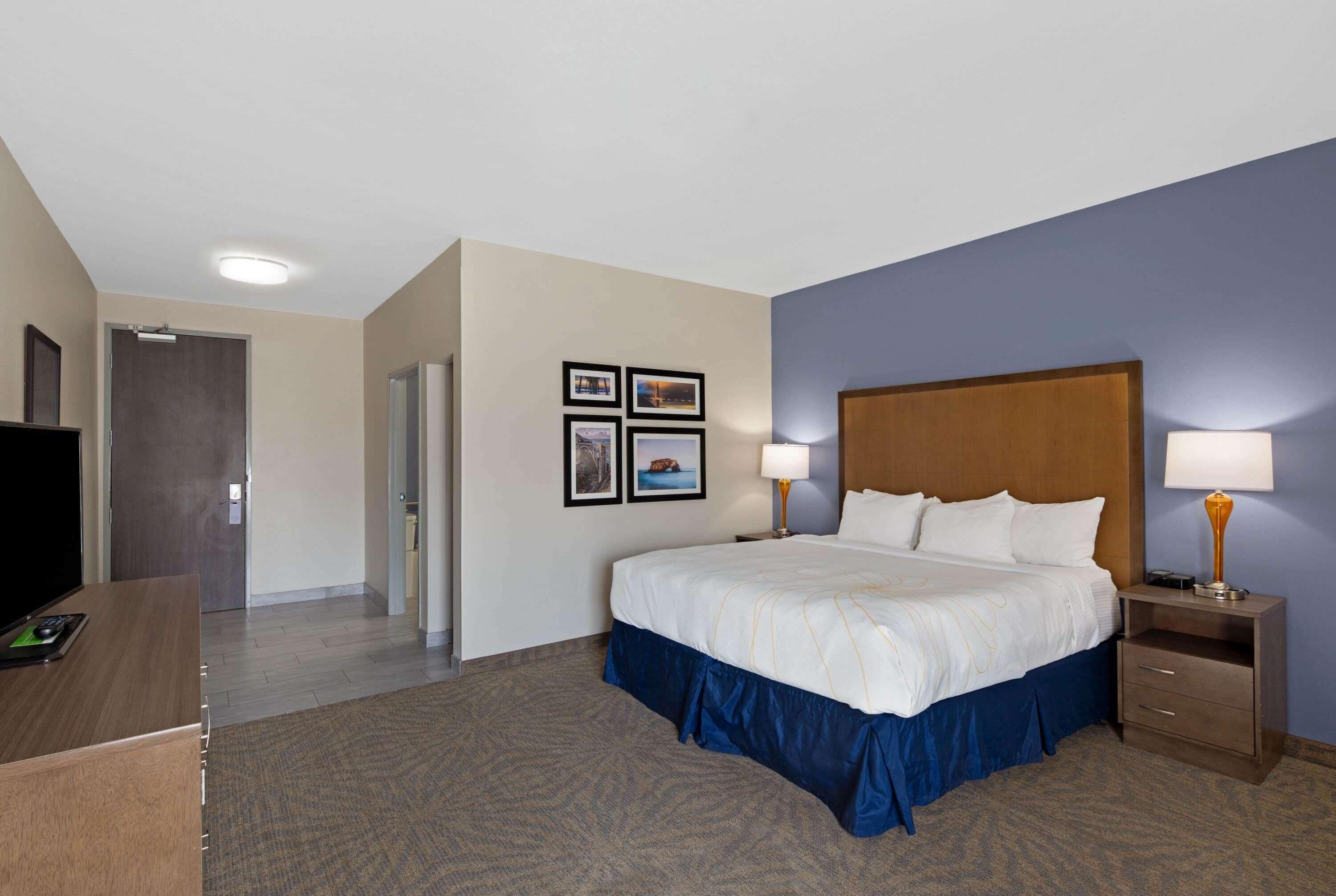 A hotel room with a large bed, bedside lamps, a desk with a computer, and a television.