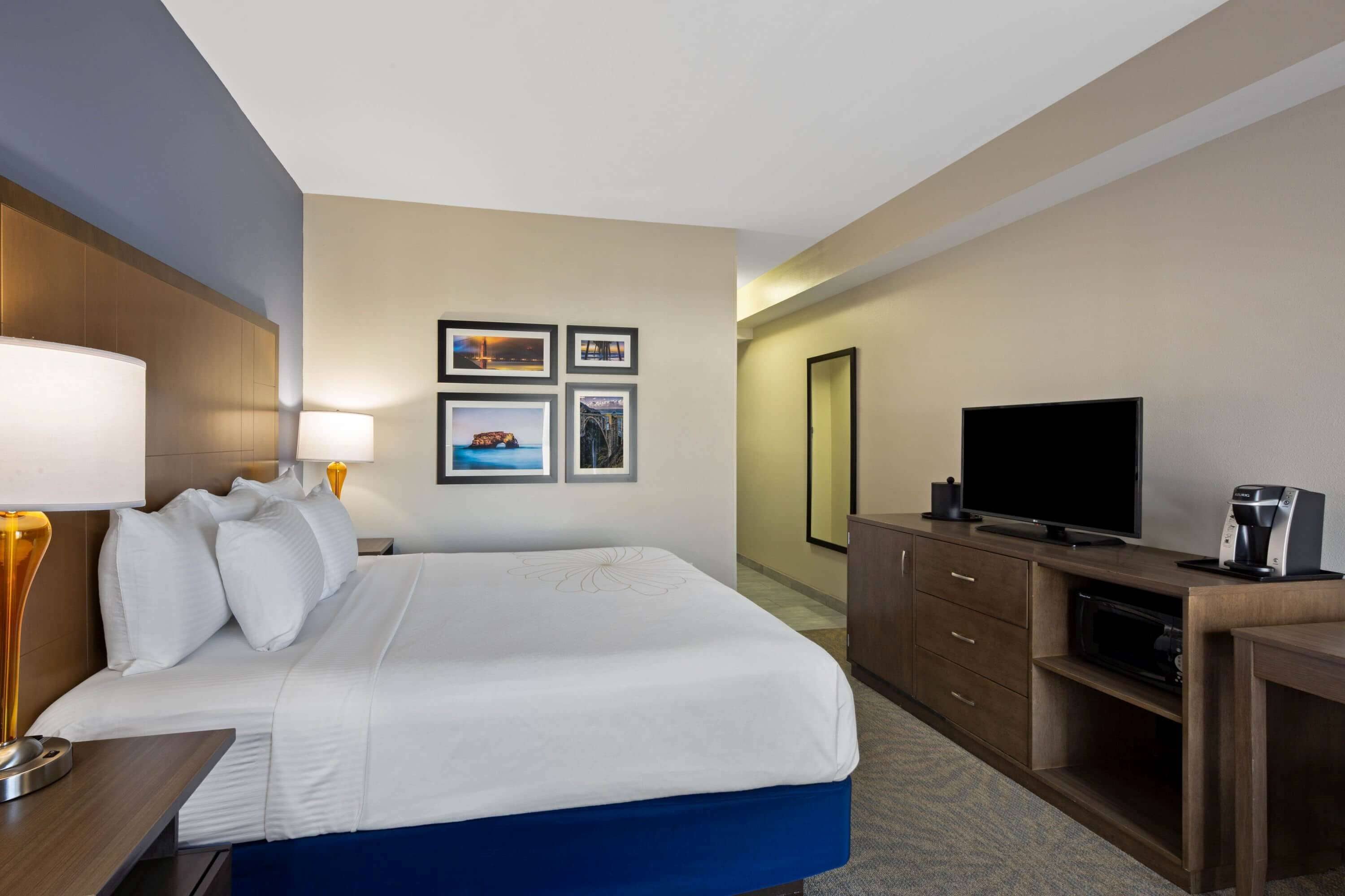 A hotel room with a bed, a desk with a lamp, a television, and a coffee maker.