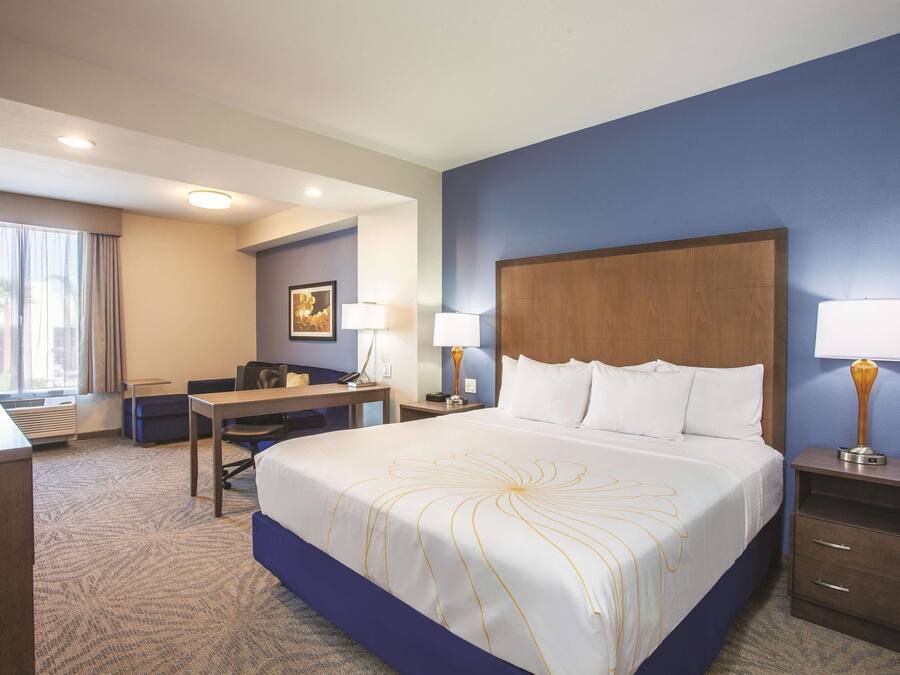 A hotel room with a large bed, a desk, a chair, a lamp, and a nightstand.