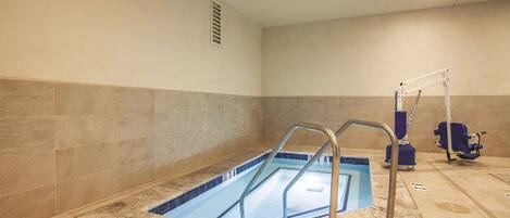 Una piscina con borde de azulejos azules, una escalera de metal y una silla azul al fondo.