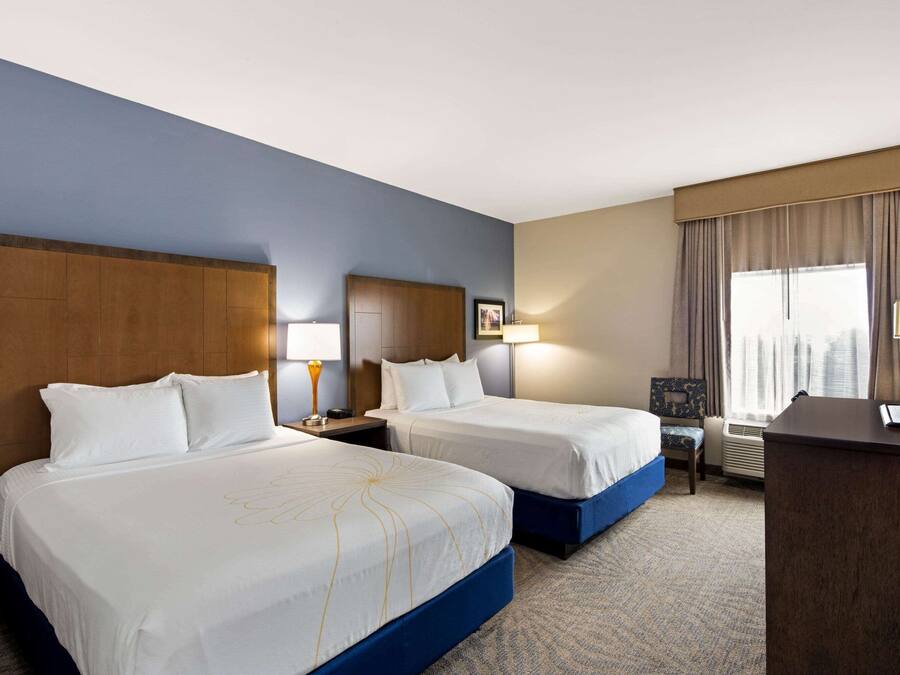 A hotel room with two beds, a desk, and a large window with curtains.