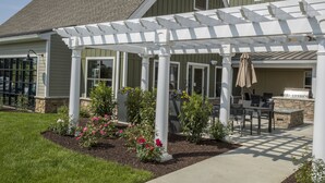 Ein überdachter Patio-Bereich mit Gartenmöbeln, einem Kamin aus Stein und einer Pergola.