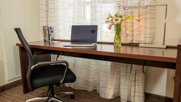 Un bureau en bois avec un ordinateur portable, une chaise de bureau noire, un vase avec des fleurs et un lampadaire.