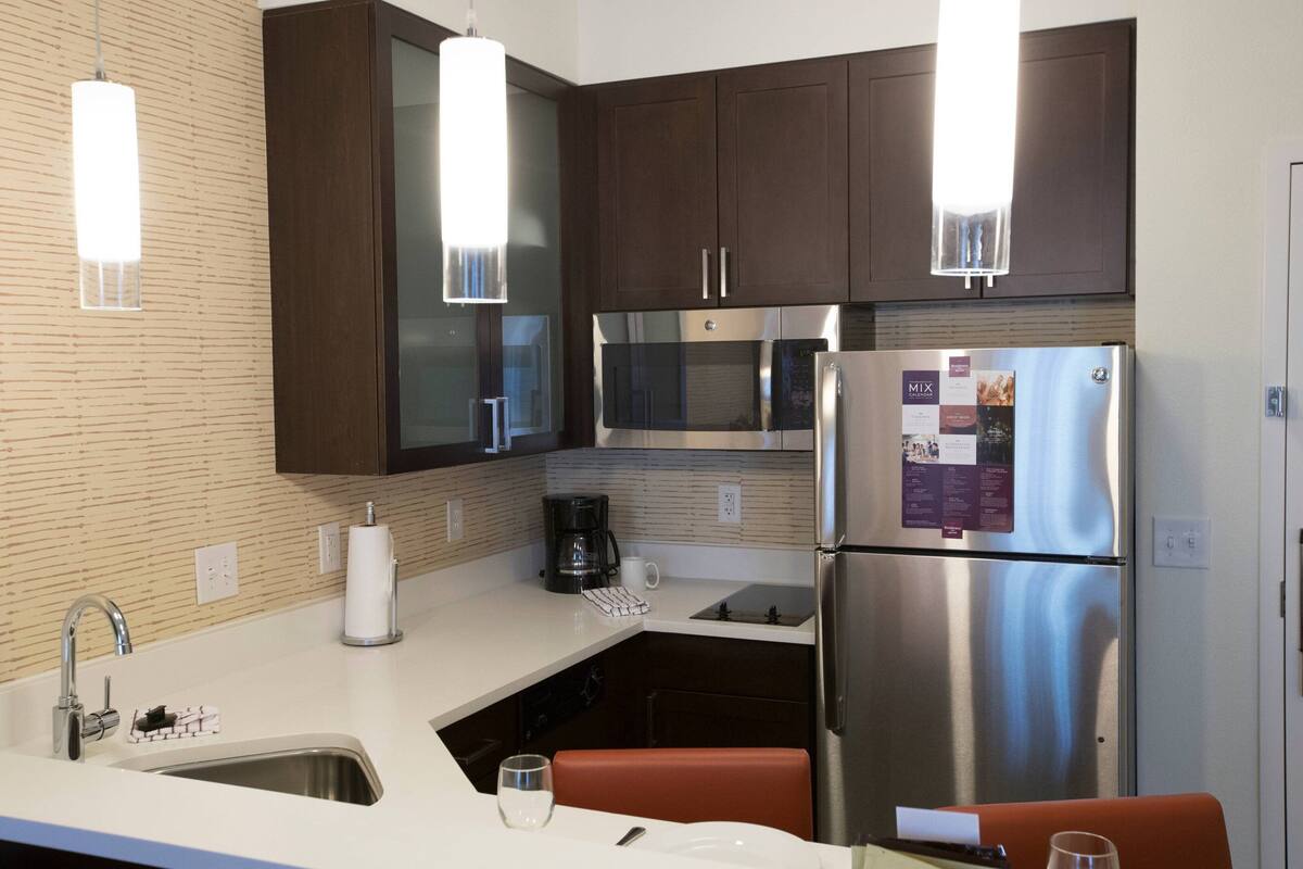 A modern kitchen with stainless steel appliances, a white countertop, and dark wooden cabinets.