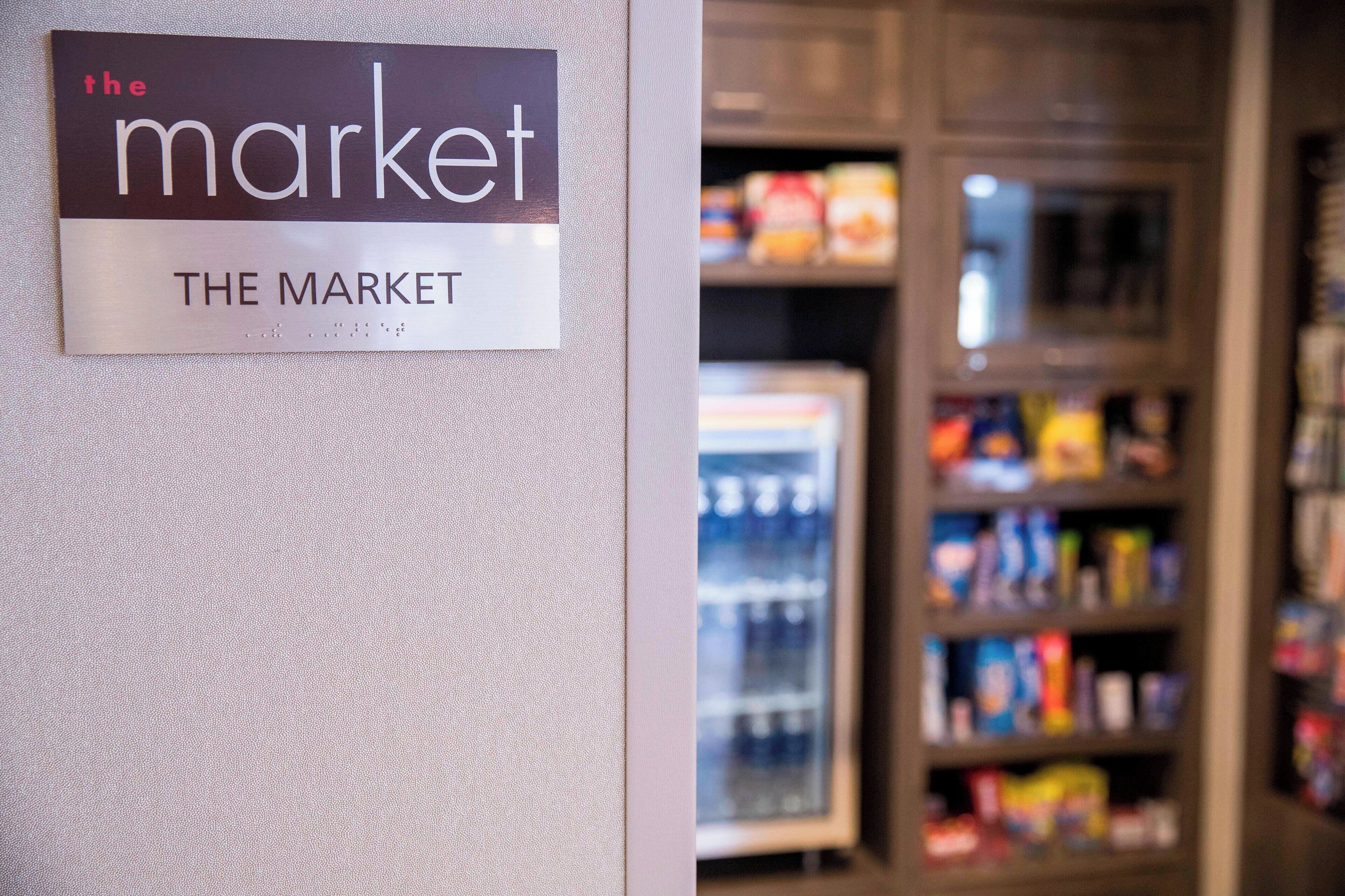 A sign for 'The Market' in a store, with shelves stocked with various products in the background.