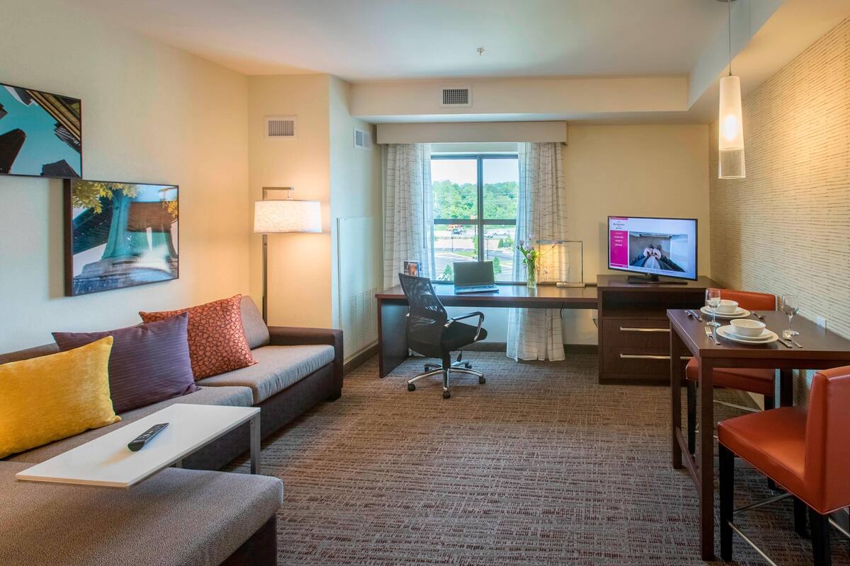 A hotel room with a sofa, a desk, a dining table, and a TV.