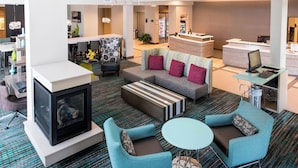Eine moderne Hotelhalle mit einer Couch, Sesseln, einem Kamin, einer Rezeption und einer Bar.