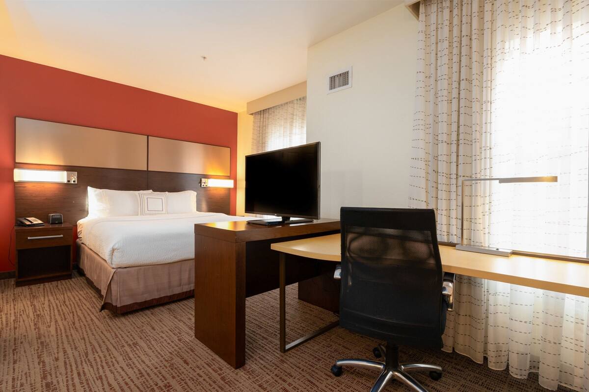A hotel room with a bed, a desk, a chair, a television, and a window with curtains.