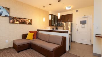 A modern kitchen with stainless steel appliances, a brown sectional sofa with cushions, and a small dining area.