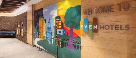 Un moderno vestíbulo de hotel con un mural de un paisaje urbano colorido, una recepción de madera y una zona de estar.