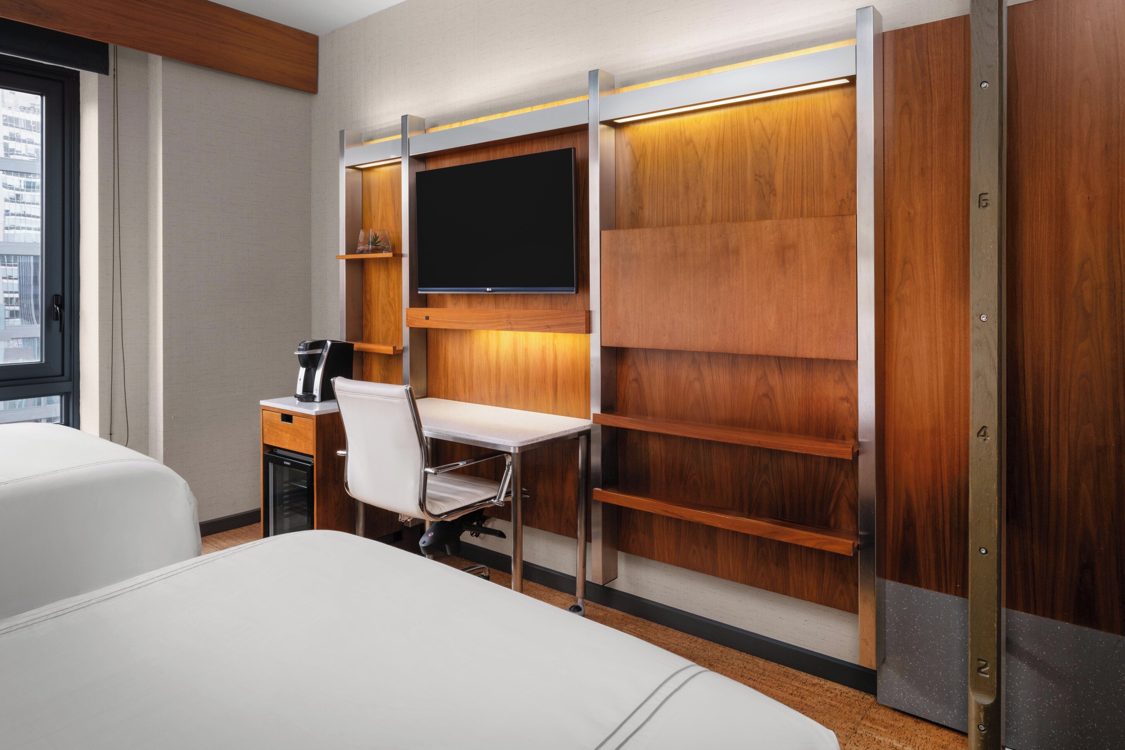 A hotel room with a bed, a desk, a chair, a television, and a minibar.